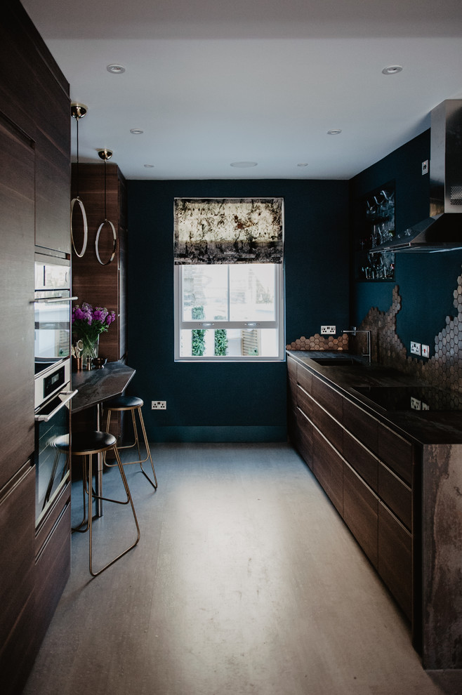 Small modern galley open plan kitchen in London with a drop-in sink, flat-panel cabinets, dark wood cabinets, solid surface benchtops, metallic splashback, metal splashback, black appliances, cork floors, no island, grey floor and multi-coloured benchtop.