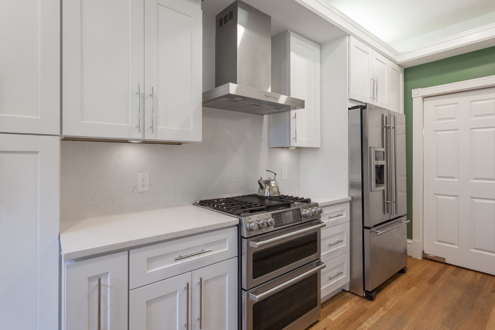 This is an example of a mid-sized transitional galley eat-in kitchen in DC Metro with an undermount sink, shaker cabinets, white cabinets, quartz benchtops, white splashback, stone slab splashback, stainless steel appliances, no island and white benchtop.