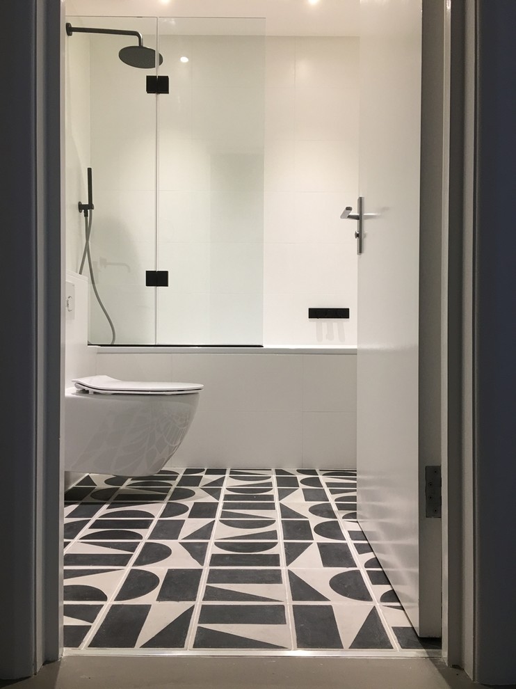 Inspiration for a small modern bathroom in London with flat-panel cabinets, a drop-in tub, a shower/bathtub combo, a wall-mount toilet, black and white tile, ceramic tile, white walls, ceramic floors, a wall-mount sink and solid surface benchtops.