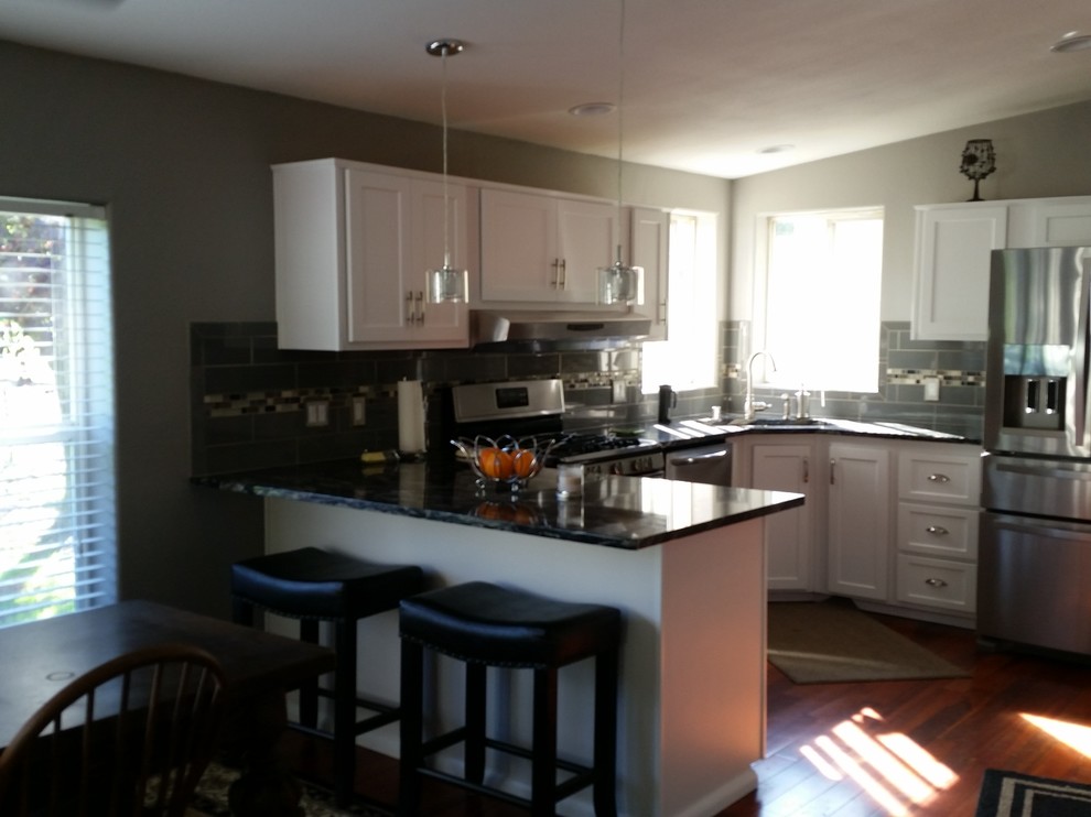 Mid-sized transitional u-shaped medium tone wood floor enclosed kitchen photo in Seattle with an undermount sink, recessed-panel cabinets, white cabinets, granite countertops, gray backsplash, ceramic backsplash, stainless steel appliances and a peninsula
