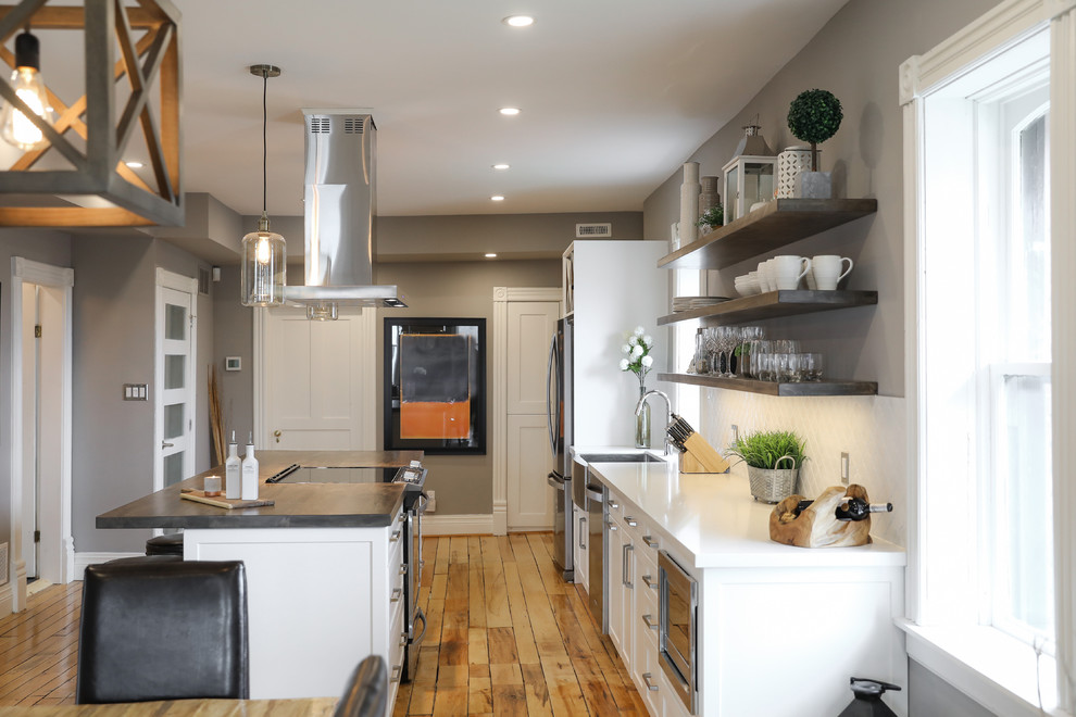 Inspiration for a mid-sized transitional single-wall medium tone wood floor and brown floor eat-in kitchen remodel with a farmhouse sink, shaker cabinets, white cabinets, white backsplash, stainless steel appliances, an island and white countertops