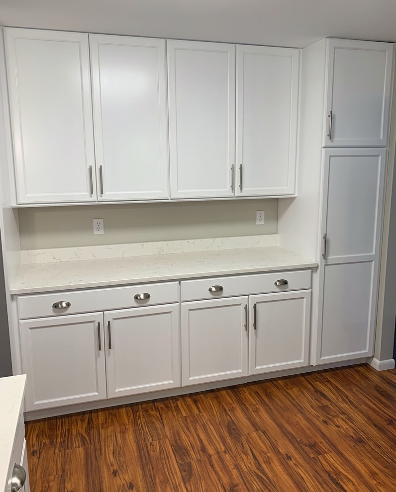 Photo of a mid-sized contemporary u-shaped separate kitchen in Burlington with an undermount sink, recessed-panel cabinets, white cabinets, stainless steel appliances, medium hardwood floors, a peninsula, brown floor and white benchtop.