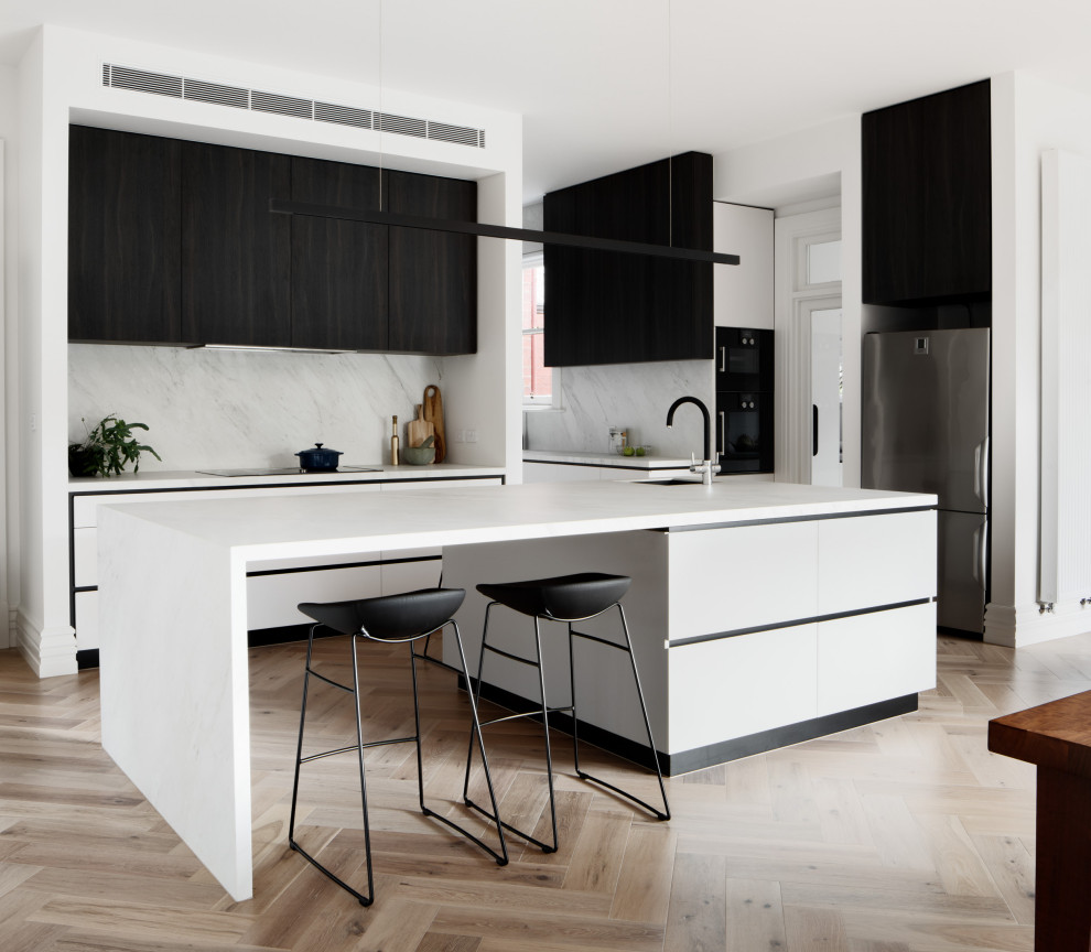 This is an example of a contemporary u-shaped eat-in kitchen in Melbourne with an undermount sink, flat-panel cabinets, grey splashback, stainless steel appliances, medium hardwood floors, with island, brown floor and white benchtop.