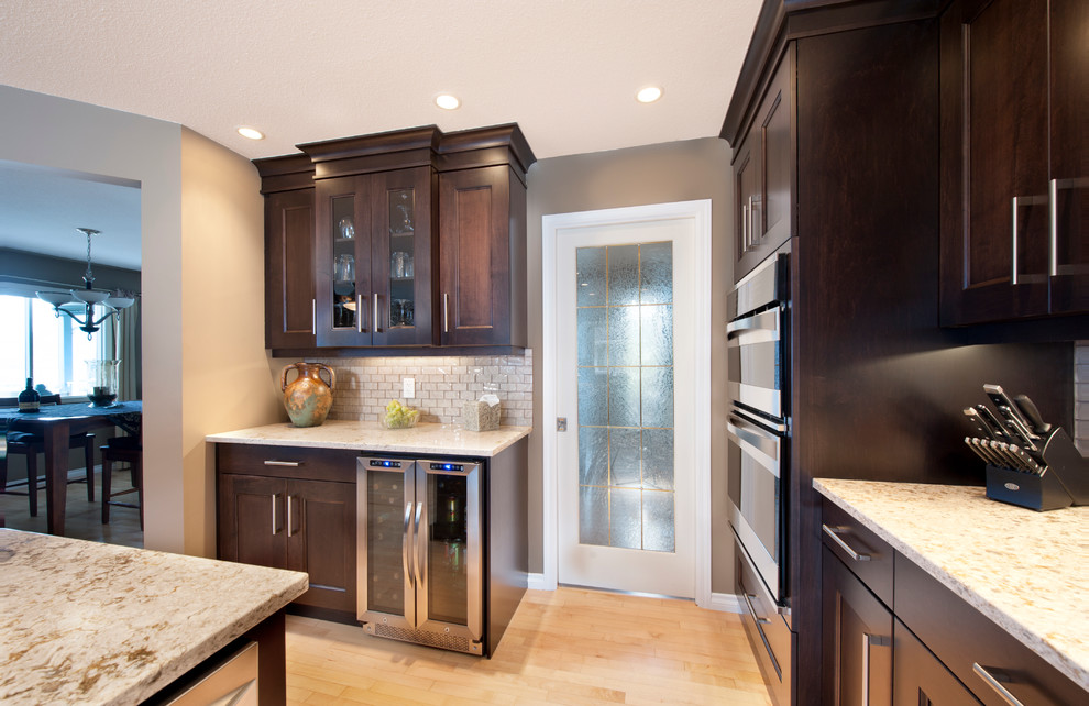 Example of a large u-shaped light wood floor eat-in kitchen design in Vancouver with an undermount sink, recessed-panel cabinets, dark wood cabinets, glass tile backsplash, stainless steel appliances and an island