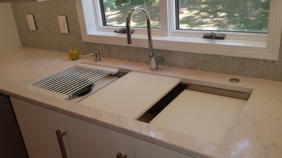Example of a small transitional galley medium tone wood floor home design design with an undermount sink, flat-panel cabinets, white cabinets, quartz countertops, white backsplash, mosaic tile backsplash and stainless steel appliances