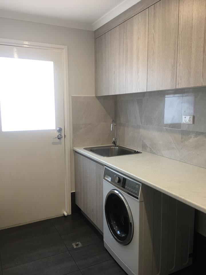 This is an example of a small modern single-wall dedicated laundry room in Brisbane with a drop-in sink, flat-panel cabinets, light wood cabinets, laminate benchtops, grey walls, ceramic floors, an integrated washer and dryer, black floor and grey benchtop.