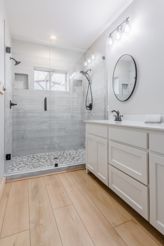 This is an example of a medium sized farmhouse ensuite bathroom in Houston with shaker cabinets, white cabinets, a walk-in shower, grey tiles, porcelain tiles, grey walls, vinyl flooring, a console sink, marble worktops, beige floors, a sliding door, white worktops, double sinks and a built in vanity unit.