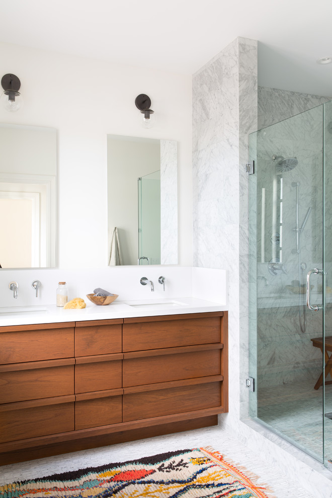 This is an example of a transitional bathroom in San Francisco with flat-panel cabinets, brown cabinets, an alcove shower, white tile, marble, white walls, an undermount sink, white floor and a hinged shower door.