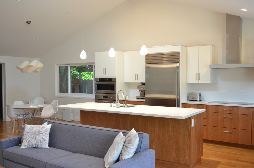 Photo of a large midcentury l-shaped open plan kitchen in San Francisco with an undermount sink, flat-panel cabinets, medium wood cabinets, quartz benchtops, white splashback, porcelain splashback, stainless steel appliances, medium hardwood floors, with island, brown floor, white benchtop and vaulted.