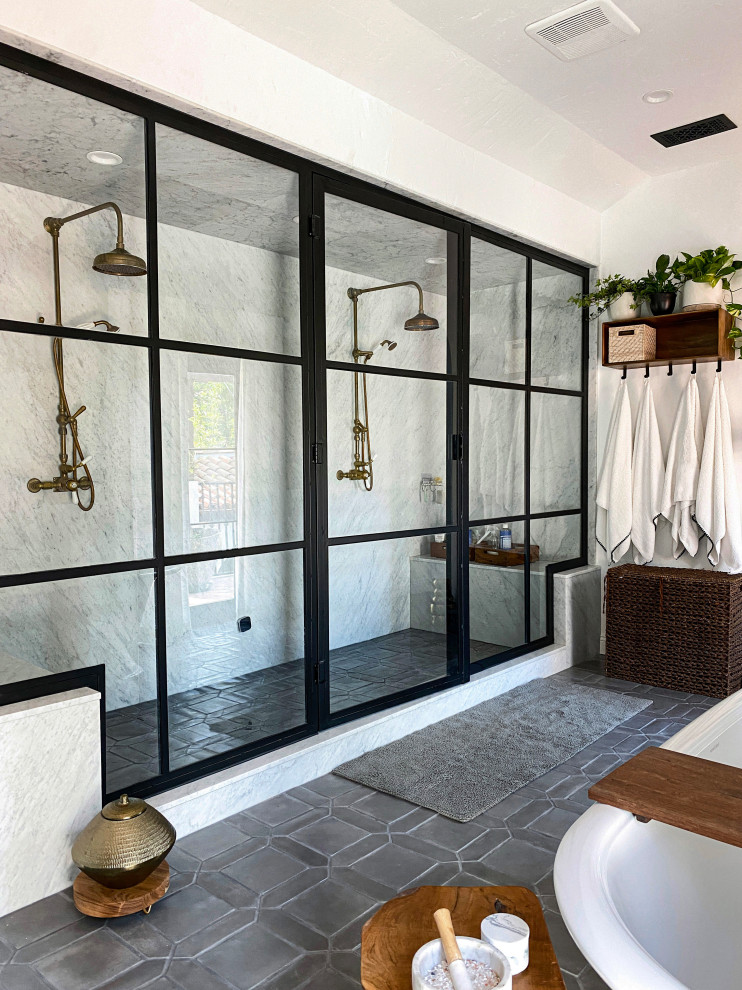 This is an example of a beach style bathroom with a freestanding tub, a double shower, white tile, white walls, grey floor and a hinged shower door.