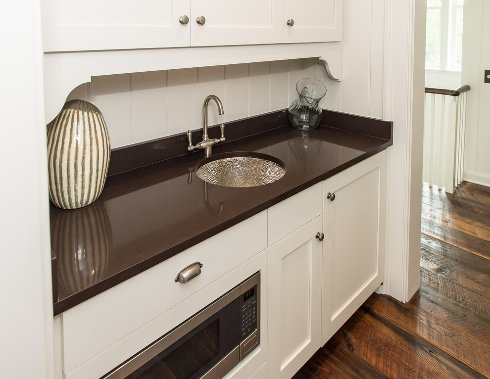 This is an example of a small traditional single-wall wet bar in Charleston with an undermount sink, shaker cabinets, beige cabinets, quartz benchtops, brown splashback, stone tile splashback and medium hardwood floors.