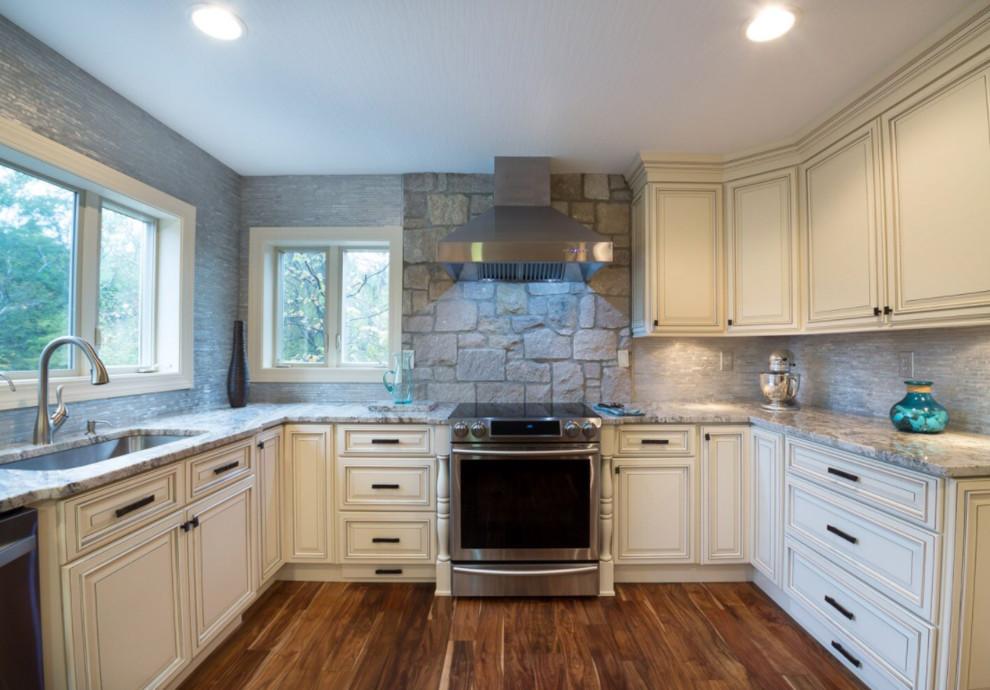 Open concept kitchen - mid-sized transitional u-shaped dark wood floor and brown floor open concept kitchen idea in Orlando with an undermount sink, recessed-panel cabinets, white cabinets, granite countertops, gray backsplash, stone tile backsplash, stainless steel appliances, an island and gray countertops