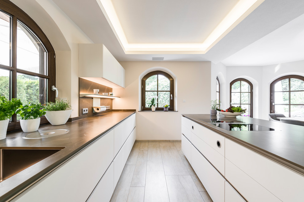 Photo of a large contemporary galley open plan kitchen in Leipzig with flat-panel cabinets, white cabinets, beige floor, a drop-in sink, white appliances, terra-cotta floors and multiple islands.