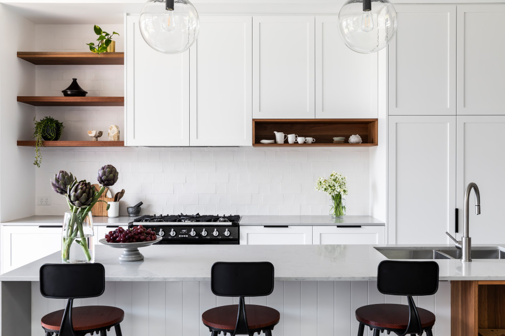Mid-sized transitional single-wall open plan kitchen in Sydney with an undermount sink, shaker cabinets, white cabinets, quartz benchtops, white splashback, ceramic splashback, black appliances, concrete floors, with island, grey floor and grey benchtop.