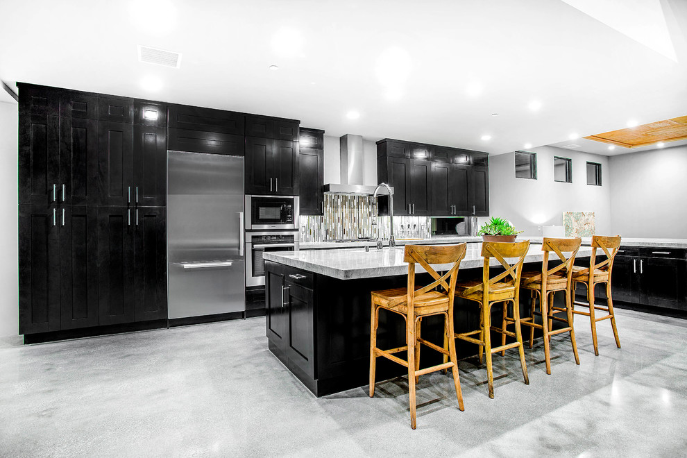 This is an example of a large modern l-shaped open plan kitchen in San Diego with an undermount sink, recessed-panel cabinets, black cabinets, marble benchtops, multi-coloured splashback, matchstick tile splashback, stainless steel appliances, concrete floors and with island.