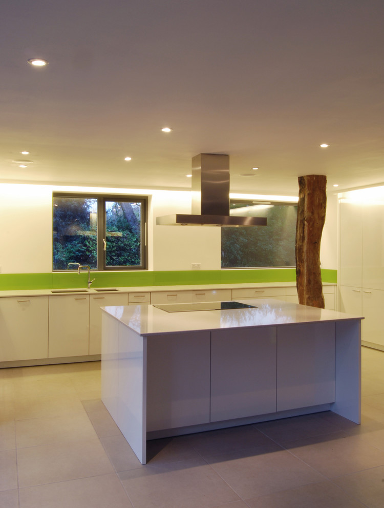 Large contemporary eat-in kitchen in London with with island, white cabinets, flat-panel cabinets, quartz benchtops, glass sheet splashback, white appliances, limestone floors, an undermount sink and green splashback.