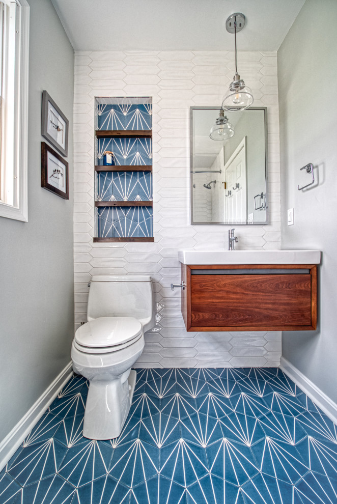 Photo of a mid-sized transitional 3/4 bathroom in Baltimore with flat-panel cabinets, medium wood cabinets, a drop-in tub, a shower/bathtub combo, a one-piece toilet, white tile, ceramic tile, grey walls, ceramic floors, an integrated sink, solid surface benchtops, blue floor, a shower curtain and white benchtops.