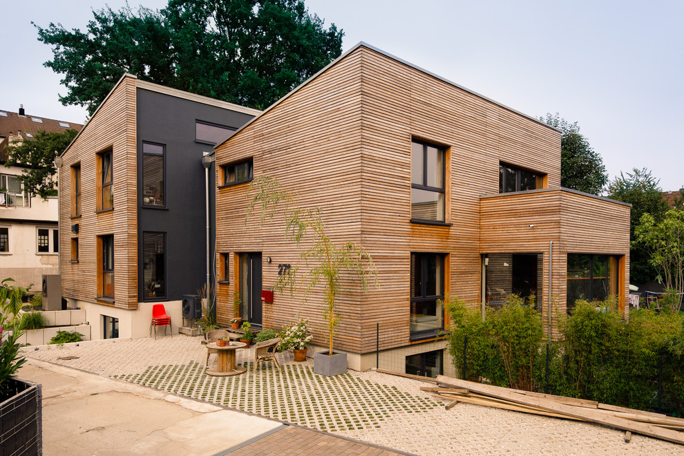 This is an example of an expansive modern two-storey brown duplex exterior in Dusseldorf with wood siding, a shed roof and clapboard siding.