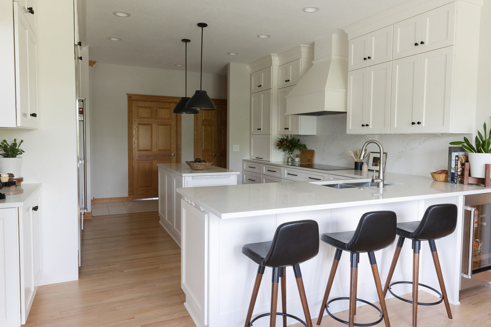 Eat-in kitchen - large transitional light wood floor eat-in kitchen idea with an undermount sink, shaker cabinets, white cabinets, quartz countertops, white backsplash, quartz backsplash, stainless steel appliances, an island and white countertops