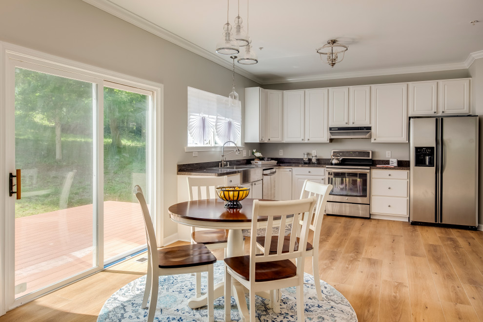 This is an example of a large contemporary l-shaped open plan kitchen in Baltimore with a farmhouse sink, stainless steel appliances, vinyl floors, no island, yellow floor, raised-panel cabinets, white cabinets and black benchtop.