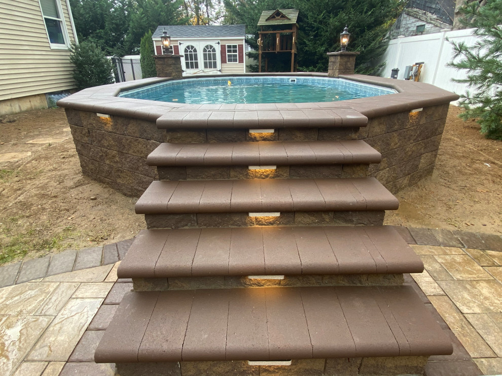 Aménagement d'un grand piscine avec aménagement paysager arrière classique sur mesure avec des pavés en béton.