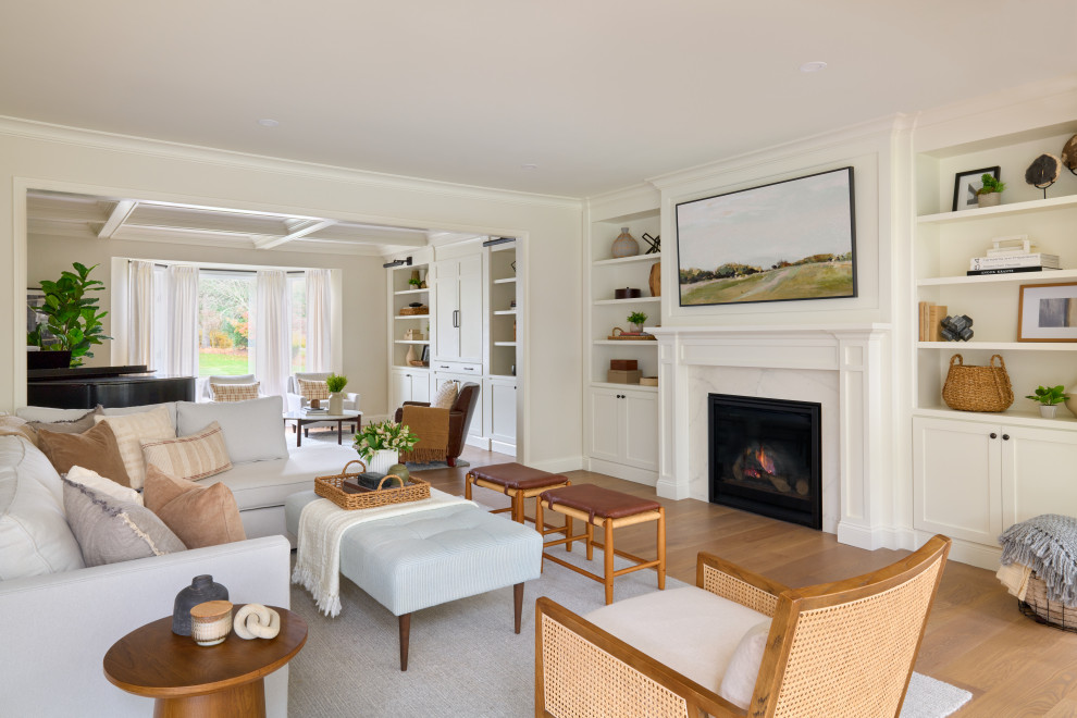 This is an example of an expansive beach style open plan games room in New York with a reading nook, white walls, a standard fireplace, a stone fireplace surround, a wall mounted tv, a coffered ceiling and medium hardwood flooring.