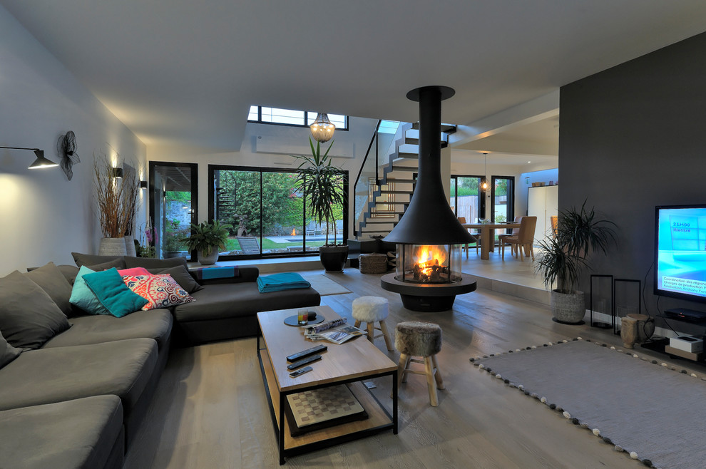 Réalisation d'un grand salon design ouvert avec un mur blanc, parquet clair, cheminée suspendue, un téléviseur fixé au mur, un manteau de cheminée en métal et un sol beige.