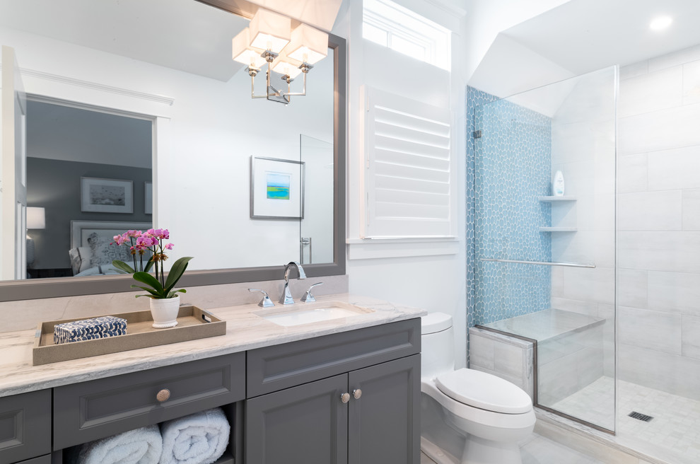Inspiration for a mid-sized beach style kids bathroom in Philadelphia with recessed-panel cabinets, grey cabinets, a one-piece toilet, blue tile, white walls, an undermount sink, marble benchtops, beige floor, a hinged shower door, beige benchtops, glass tile and marble floors.
