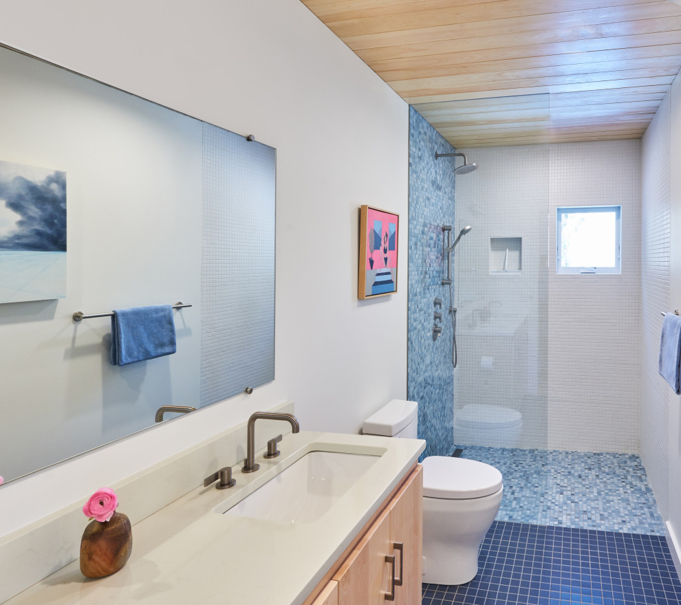 Example of a mid-sized mountain style blue tile and mosaic tile porcelain tile, blue floor, double-sink and wood ceiling bathroom design with flat-panel cabinets, light wood cabinets, a one-piece toilet, white walls, an undermount sink, quartzite countertops, white countertops, a niche and a built-in vanity