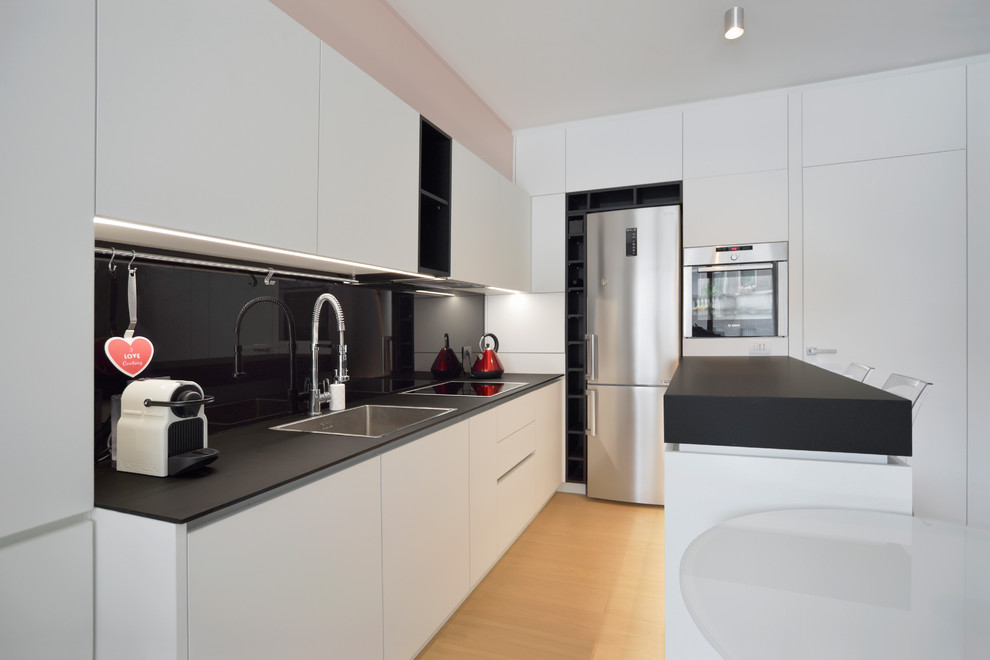 This is an example of a small contemporary u-shaped open plan kitchen in Milan with a drop-in sink, black splashback, light hardwood floors, a peninsula and black benchtop.