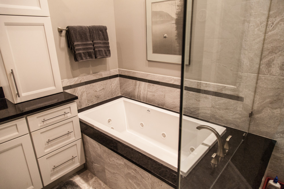 Inspiration for a mid-sized transitional master gray tile and ceramic tile marble floor, gray floor and double-sink drop-in bathtub remodel with shaker cabinets, white cabinets, a two-piece toilet, gray walls, an undermount sink, quartzite countertops, a hinged shower door, black countertops, a niche and a floating vanity