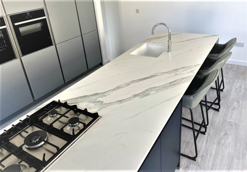 Inspiration for a mid-sized modern single-wall eat-in kitchen in Other with an undermount sink, flat-panel cabinets, grey cabinets, quartzite benchtops, black appliances, light hardwood floors, with island, grey floor and white benchtop.