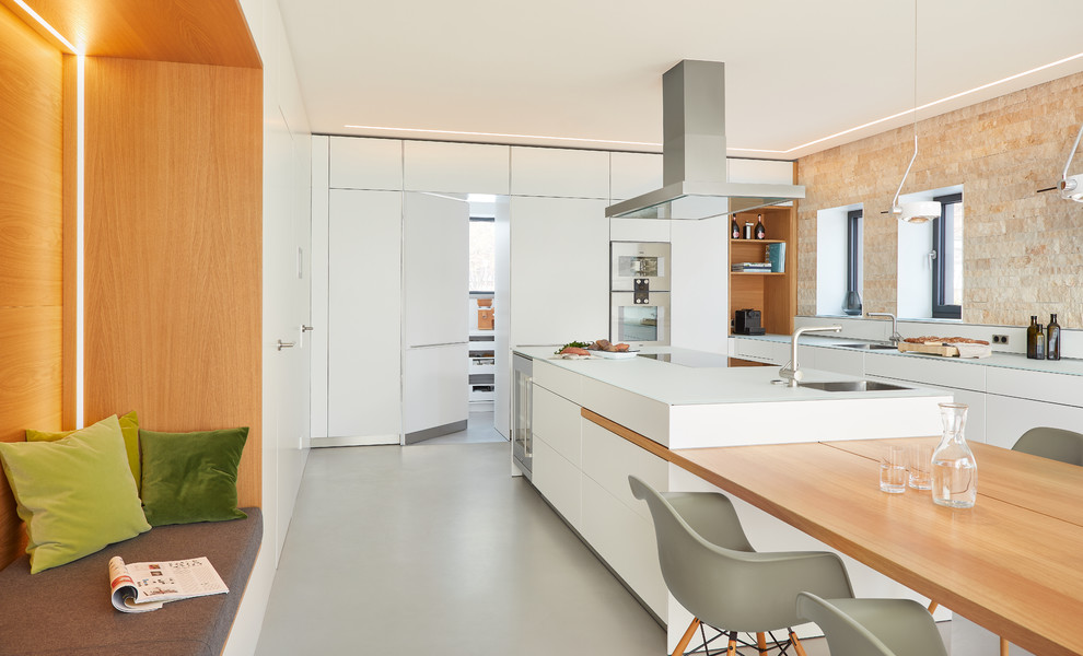 Design ideas for a large contemporary l-shaped eat-in kitchen in Stuttgart with an integrated sink, flat-panel cabinets, white cabinets, glass benchtops, beige splashback, stone slab splashback, vinyl floors, with island, grey floor and white benchtop.