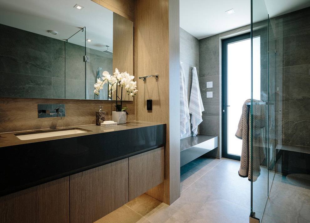 Inspiration for a large contemporary bathroom in Vancouver with flat-panel cabinets, medium wood cabinets, a curbless shower, gray tile, porcelain tile, grey walls, porcelain floors, an undermount sink, engineered quartz benchtops, grey floor, a hinged shower door and grey benchtops.