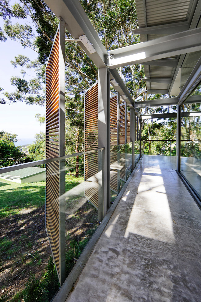 Photo of a large contemporary side yard screened-in verandah in Sydney with a roof extension, glass railing and concrete slab.