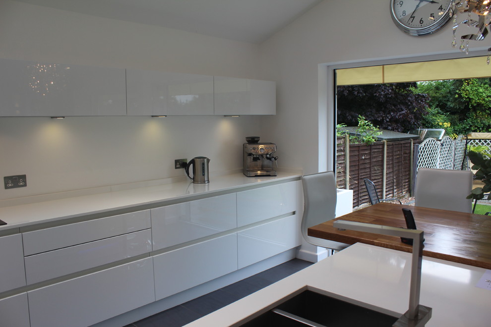This is an example of a mid-sized modern eat-in kitchen in Hertfordshire with an undermount sink, flat-panel cabinets, white cabinets, quartz benchtops, stainless steel appliances, porcelain floors and with island.