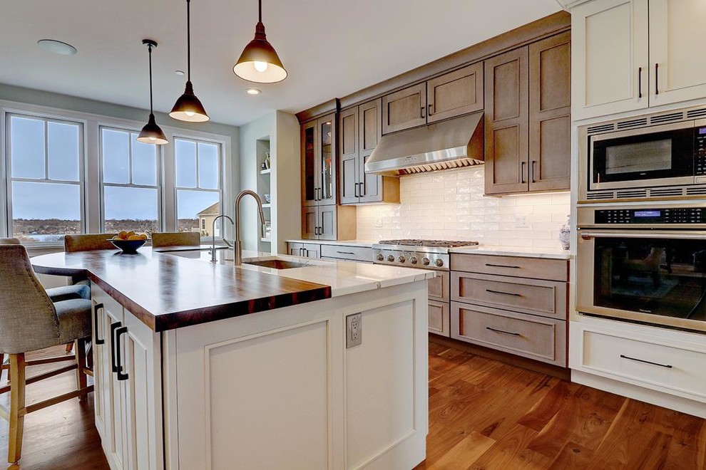 Large transitional galley eat-in kitchen in Providence with an undermount sink, flat-panel cabinets, white cabinets, quartz benchtops, white splashback, subway tile splashback, stainless steel appliances, medium hardwood floors, with island and brown floor.