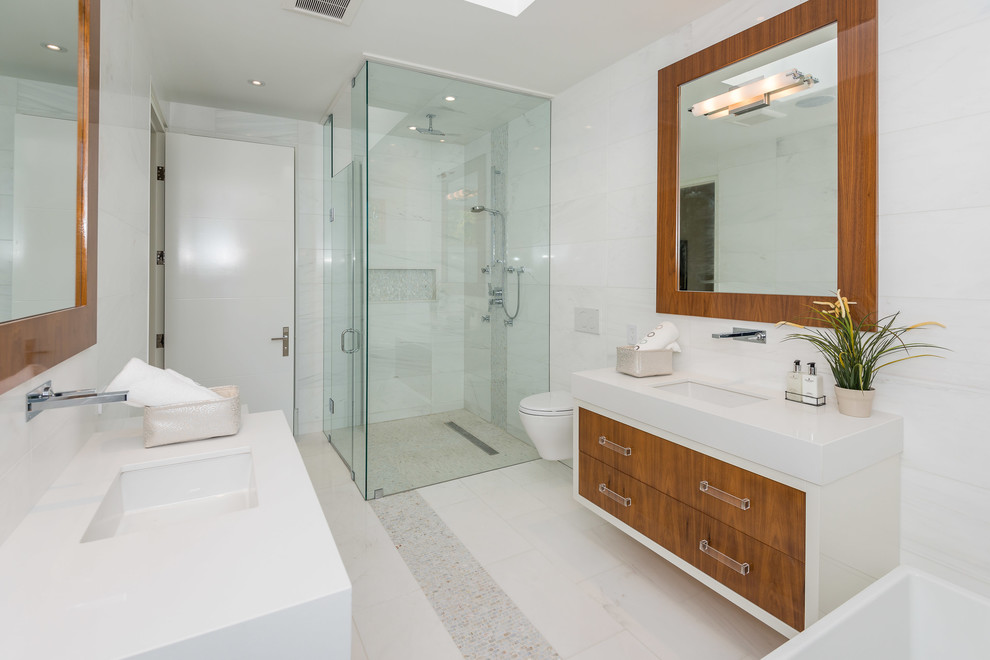 This is an example of a large modern master bathroom in Toronto with flat-panel cabinets, dark wood cabinets, a freestanding tub, a corner shower, a wall-mount toilet, white tile, porcelain tile, white walls, porcelain floors, an undermount sink, engineered quartz benchtops, white floor and a hinged shower door.