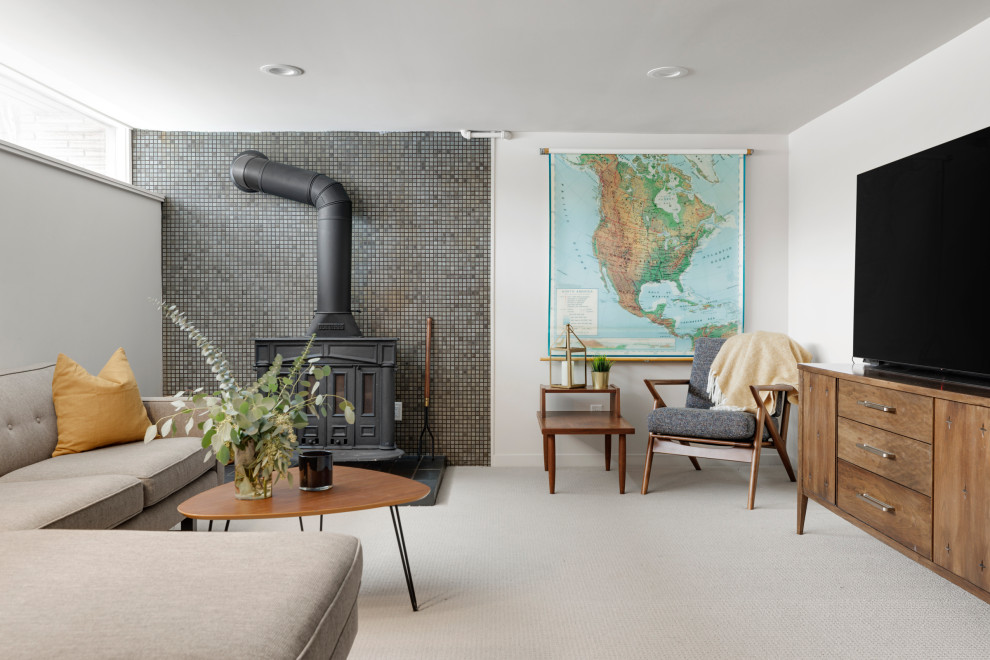 Cette photo montre une salle de séjour rétro de taille moyenne et fermée avec un mur blanc, moquette, un poêle à bois, un manteau de cheminée en carrelage, un téléviseur fixé au mur et un sol gris.