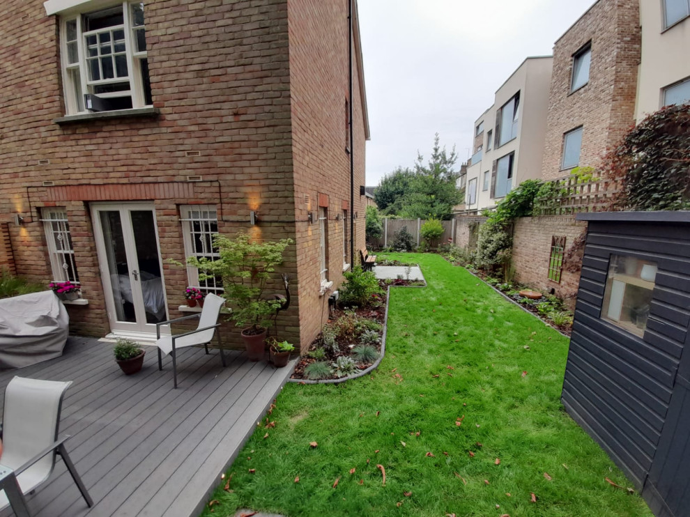 This is an example of a medium sized contemporary back partial sun garden wall in London with a flowerbed and decking.