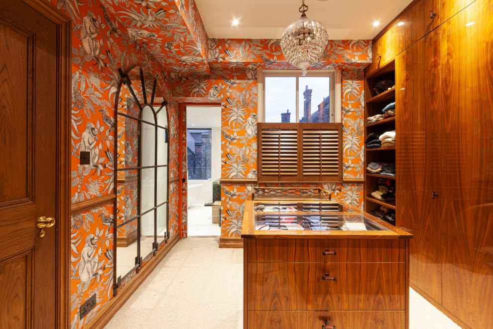 Large eclectic gender-neutral walk-in wardrobe in London with flat-panel cabinets, medium wood cabinets, carpet, beige floor and wallpaper.