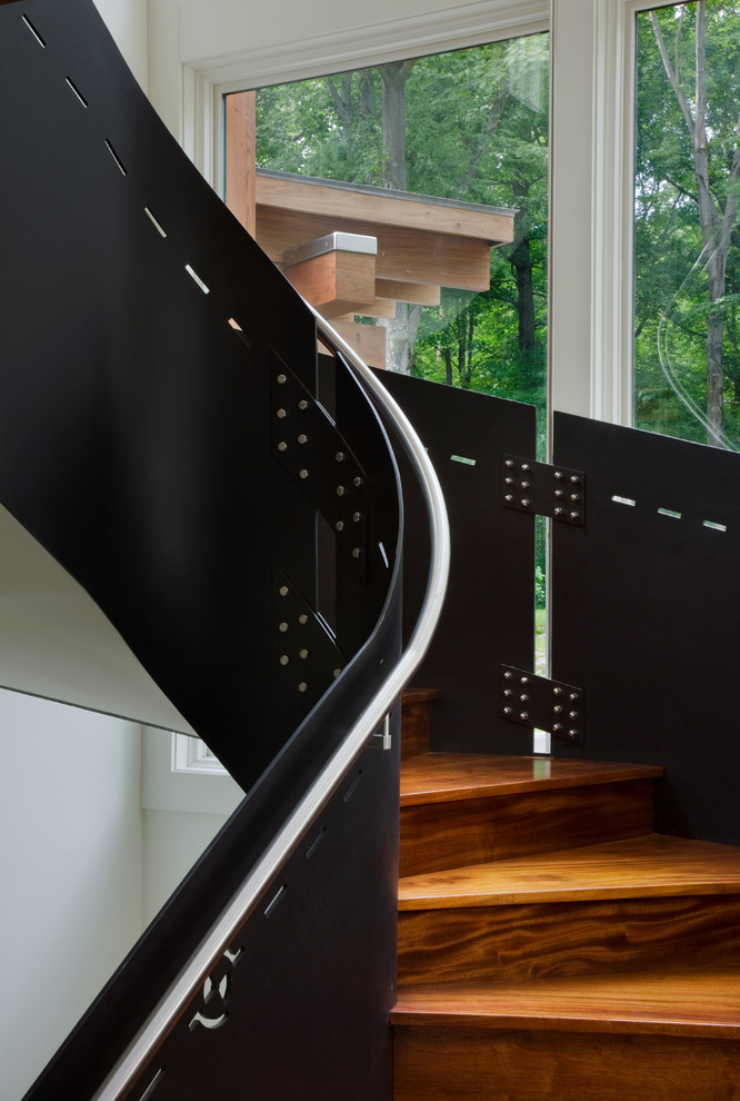 Contemporary wood curved staircase in New York with wood risers and metal railing.
