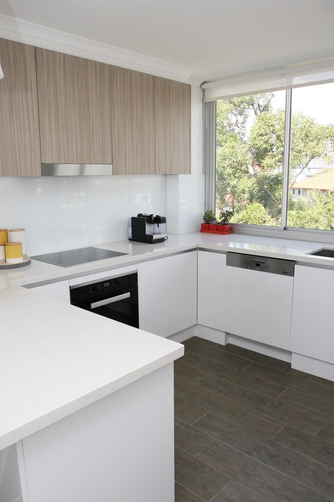 Photo of a mid-sized contemporary u-shaped eat-in kitchen in Sydney with an undermount sink, flat-panel cabinets, quartz benchtops, white splashback, glass sheet splashback, stainless steel appliances, dark hardwood floors, white cabinets, a peninsula, brown floor and white benchtop.
