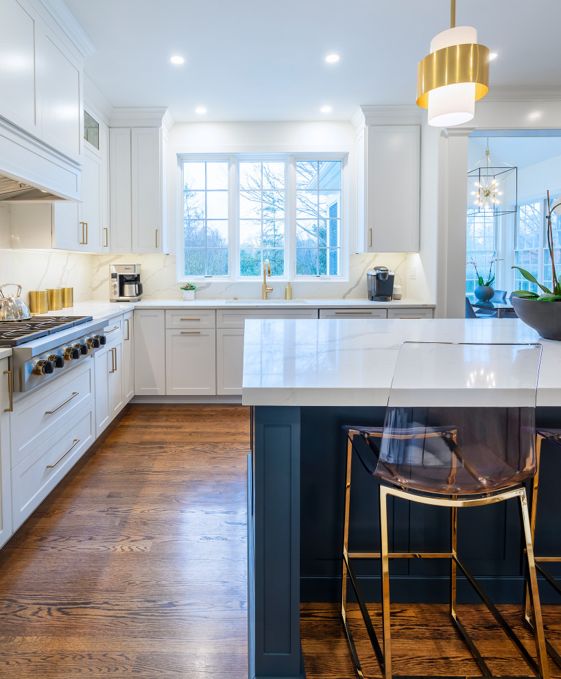 This is an example of a large transitional kitchen in Philadelphia with an undermount sink, shaker cabinets, white cabinets, quartz benchtops, white splashback, engineered quartz splashback, stainless steel appliances, dark hardwood floors, with island, brown floor and white benchtop.