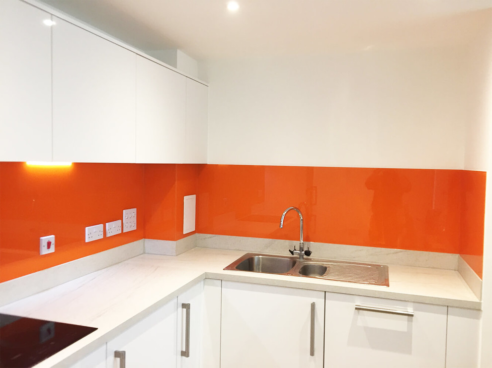 This is an example of a large modern eat-in kitchen in Hertfordshire with flat-panel cabinets, white cabinets, marble benchtops, orange splashback, glass sheet splashback and no island.