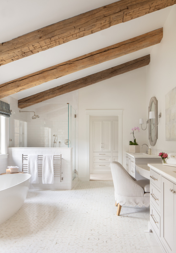 This is an example of a large farmhouse ensuite bathroom in Santa Barbara with recessed-panel cabinets, grey cabinets, a freestanding bath, white walls, a submerged sink, white floors, a hinged door, white worktops, a single sink, a built in vanity unit, exposed beams, a vaulted ceiling, a corner shower and white tiles.