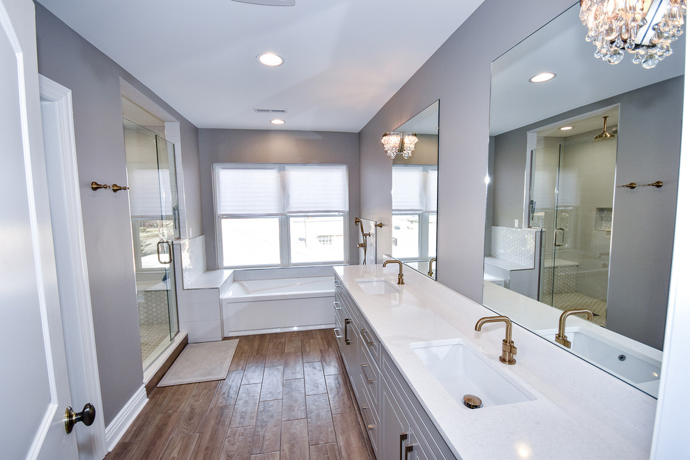 This is an example of a large contemporary master bathroom in Chicago with shaker cabinets, grey cabinets, an undermount tub, a shower/bathtub combo, a one-piece toilet, white tile, ceramic tile, grey walls, medium hardwood floors, an undermount sink, engineered quartz benchtops, brown floor and a hinged shower door.