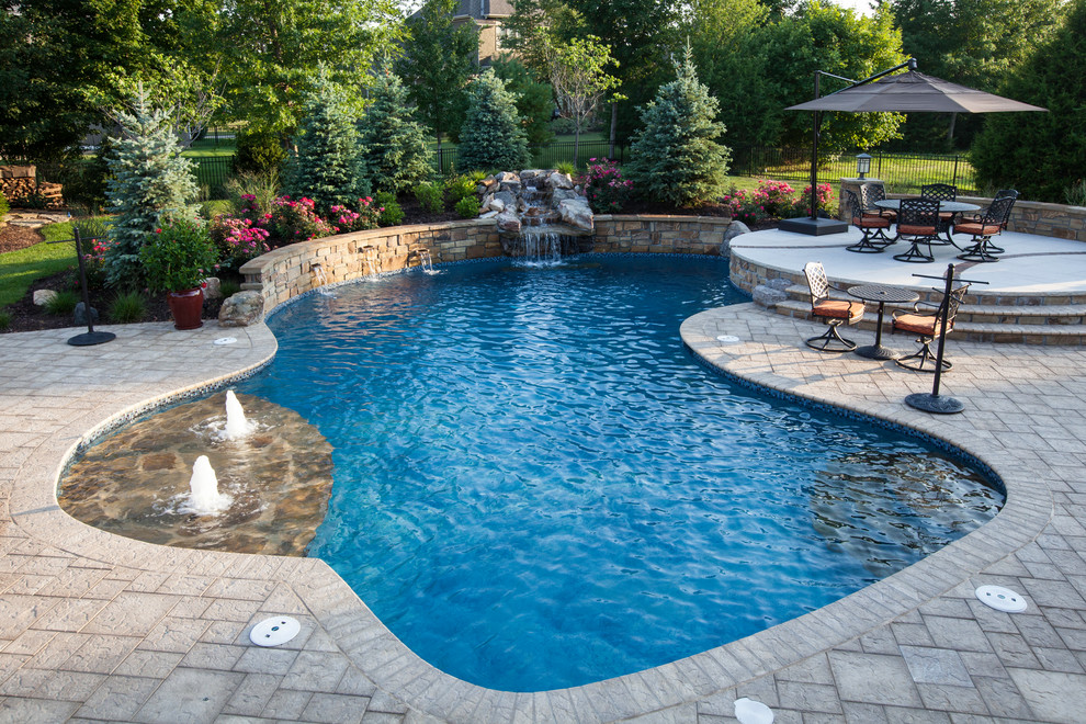 Mid-sized traditional backyard custom-shaped pool in Kansas City with a water feature and natural stone pavers.