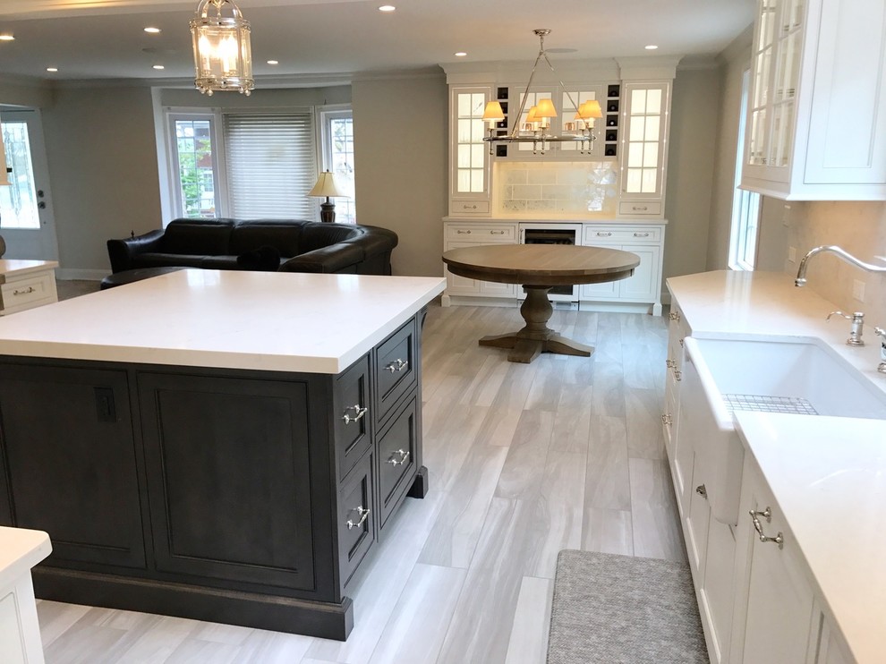 Inspiration for a mid-sized transitional u-shaped light wood floor and brown floor open concept kitchen remodel with a farmhouse sink, recessed-panel cabinets, white cabinets, marble countertops, white backsplash, marble backsplash, stainless steel appliances and an island