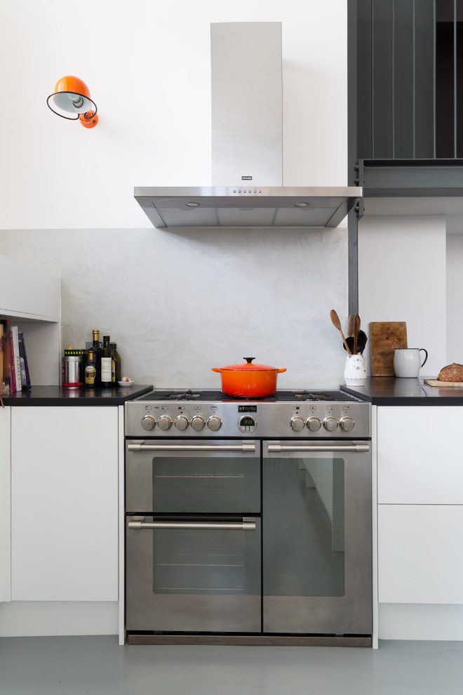 Large eclectic u-shaped eat-in kitchen in London with an undermount sink, flat-panel cabinets, white cabinets, solid surface benchtops, grey splashback, stainless steel appliances, painted wood floors and with island.